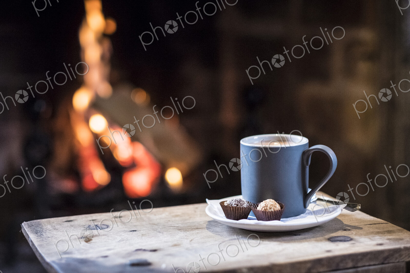 Close up of mug with hot drink on wooden table in front of fireplace.