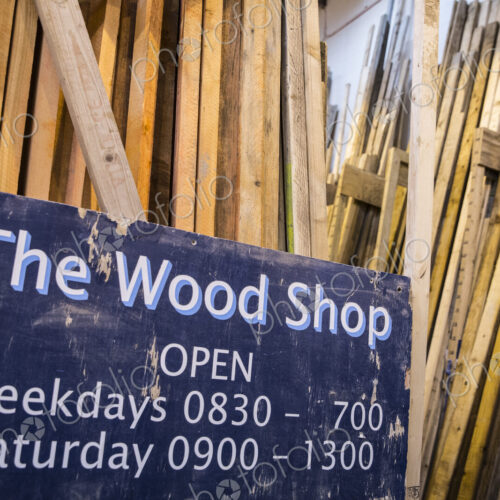 Close up of old blue Open sign for Wood Shop leaning against a stack of wooden planks. Close up of old blue Open sign for Wood Shop leaning against a stack of wooden planks.