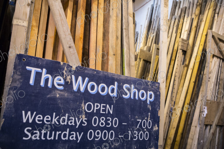 Close up of old blue Open sign for Wood Shop leaning against a stack of wooden planks.