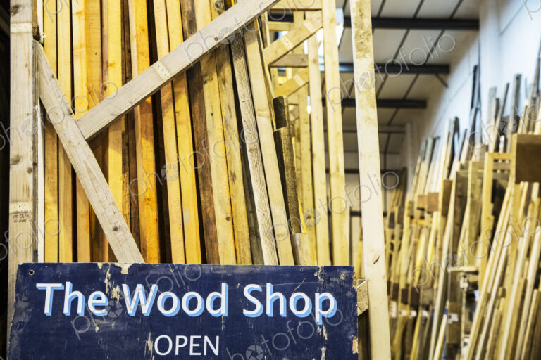 Close up of old blue Open sign for Wood Shop leaning against a stack of wooden planks.