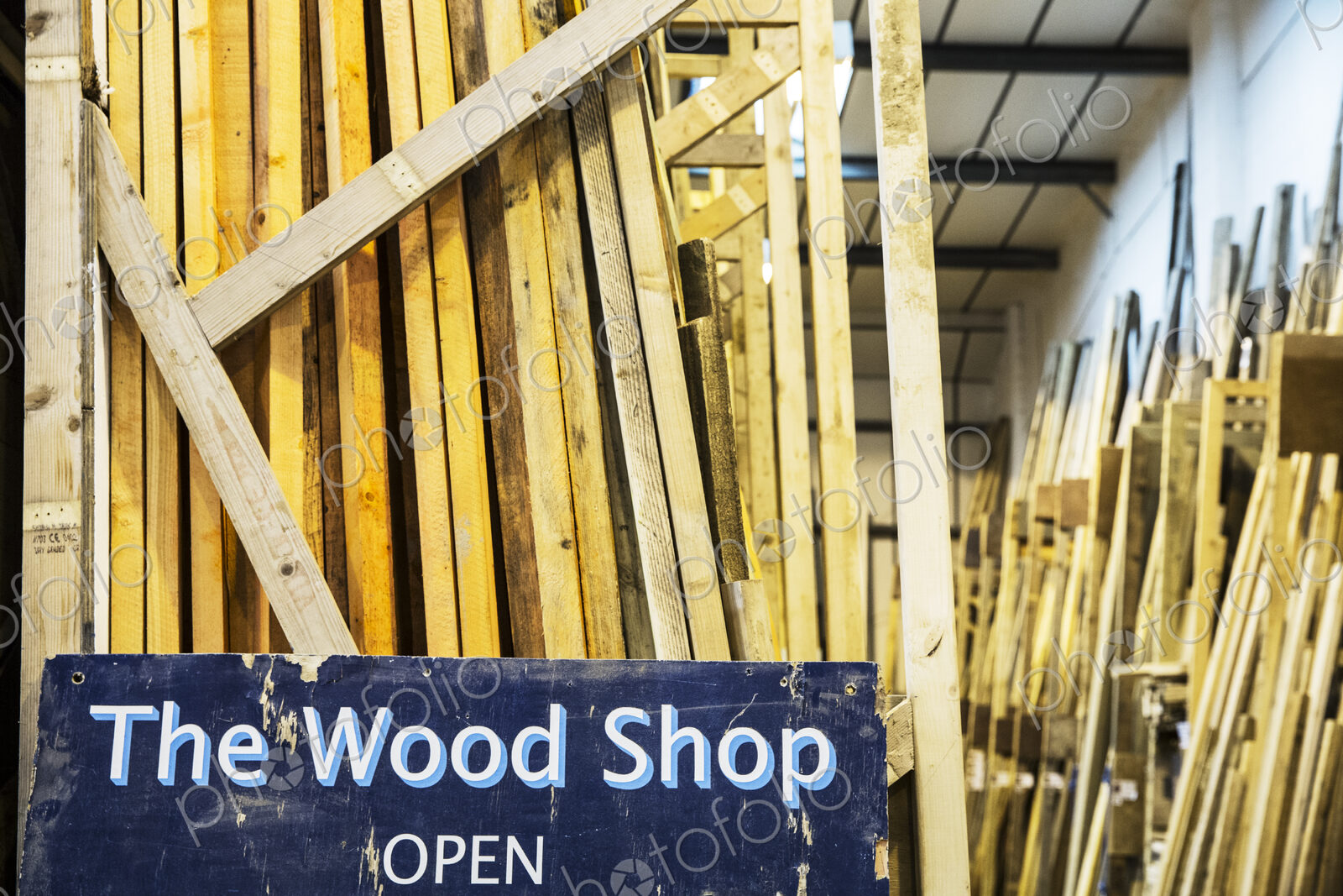 Close up of old blue Open sign for Wood Shop leaning against a stack of wooden planks.
