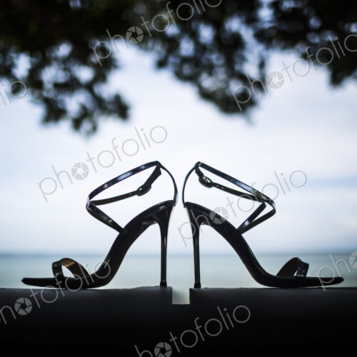 Close up of pair of shiny stiletto sandals, tree foliage and ocean in background. Close up of pair of shiny stiletto sandals, tree foliage and ocean in background.