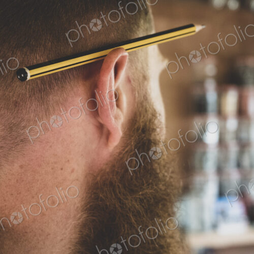 Close up of pencil over ear of bearded man with light brown hair. Close up of pencil over ear of bearded man with light brown hair.