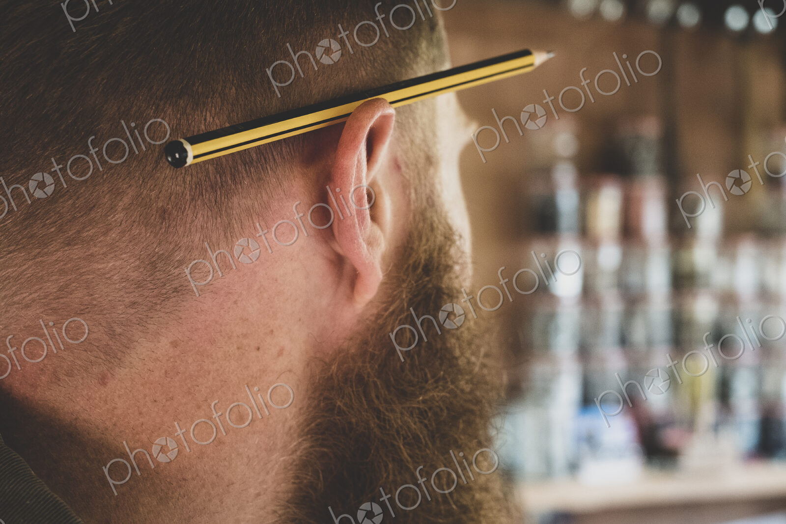 Close up of pencil over ear of bearded man with light brown hair.