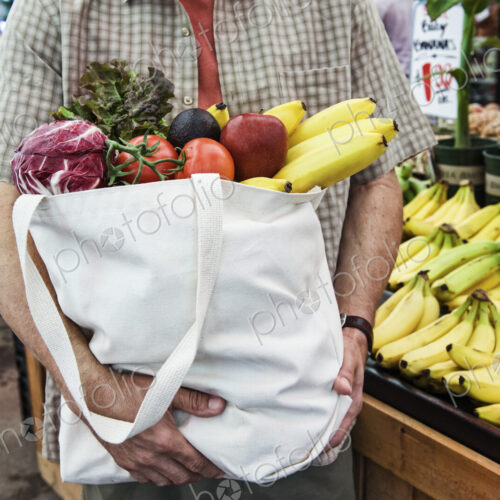 Close up of person at a food and vegetable market, holding shopping bag with fresh…