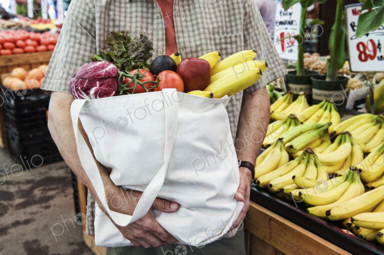 Close up of person at a food and vegetable market, holding shopping bag with fresh…