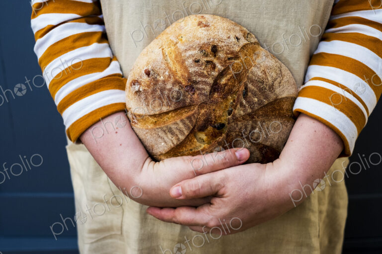 Close up of person holding a freshly baked round loaf of bread.