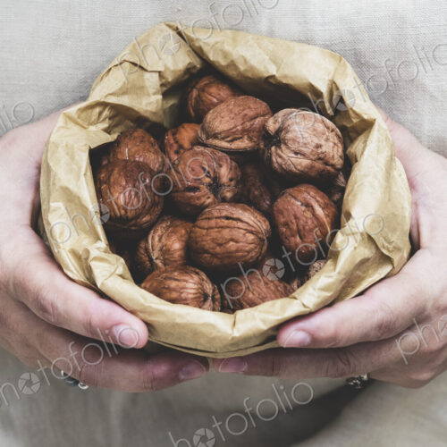 Close up of person holding brown paper bag with fresh walnuts. Close up of person holding brown paper bag with fresh walnuts.