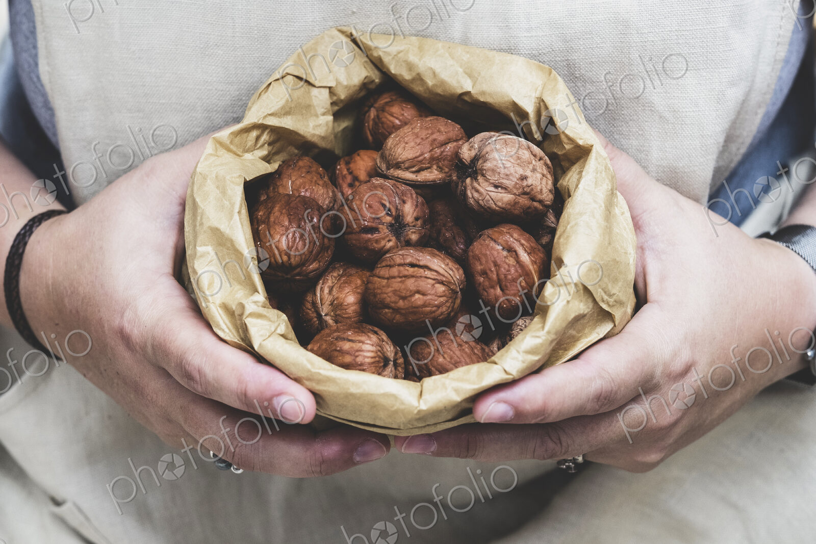 Close up of person holding brown paper bag with fresh walnuts.