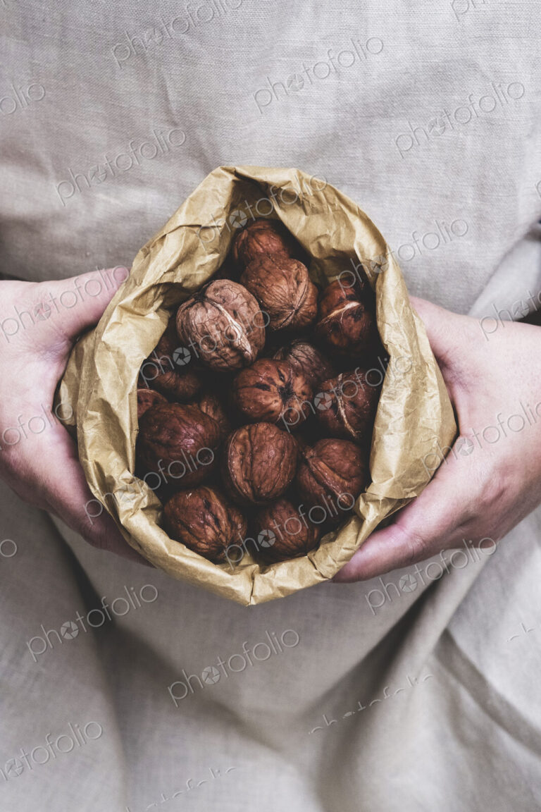 Close up of person holding brown paper bag with fresh walnuts.