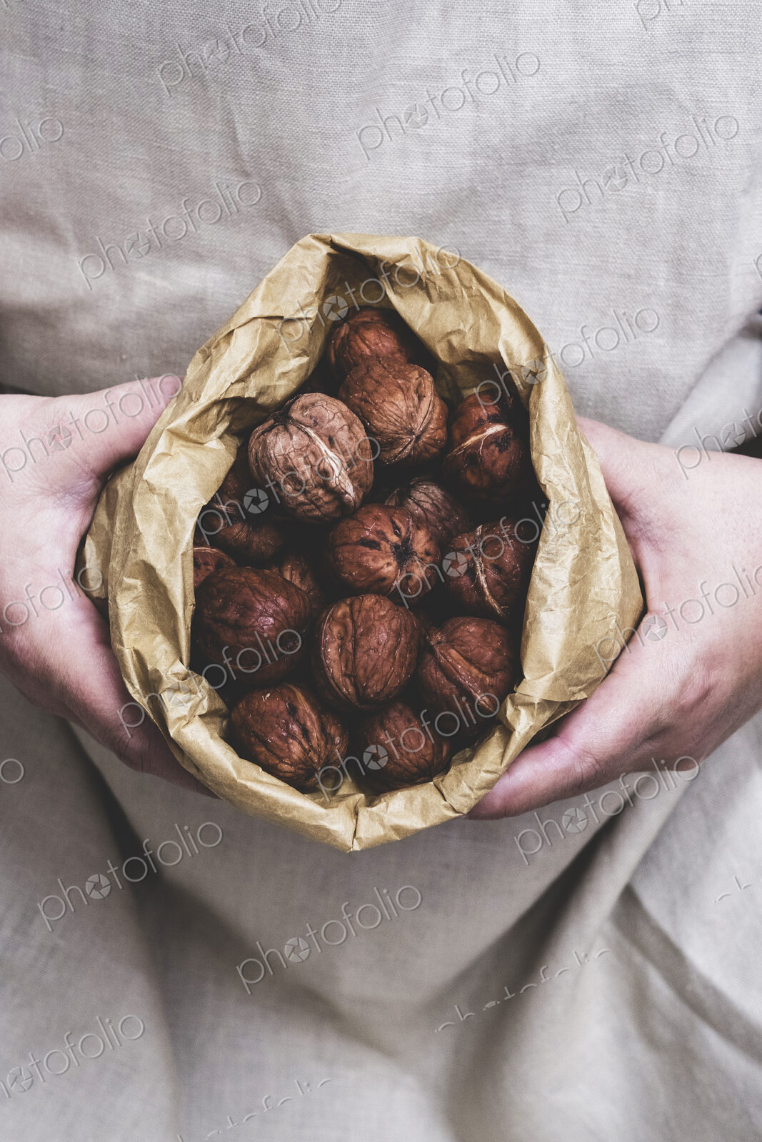 Close up of person holding brown paper bag with fresh walnuts.