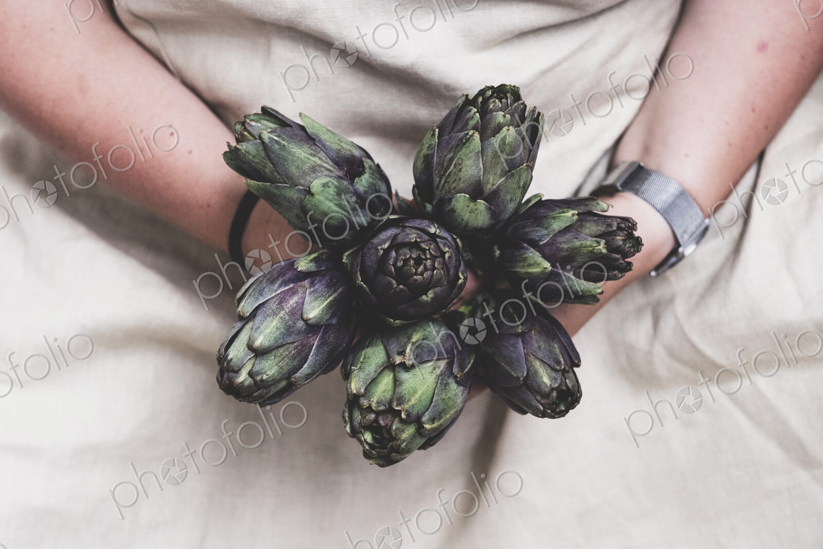 Close up of person holding bunch of fresh artichokes.