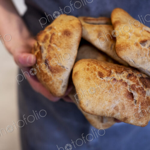 Close up of person holding freshly baked bread rolls in an artisan bakery.