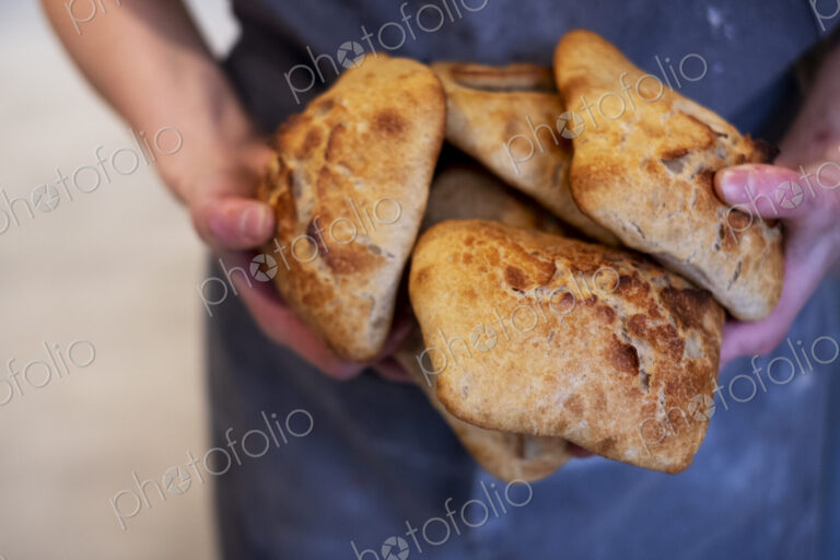 Close up of person holding freshly baked bread rolls in an artisan bakery.