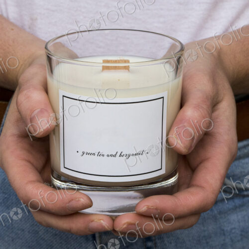 Close up of person holding handmade white and yellow jar candle with wooden wick. Close up of person holding handmade white and yellow jar candle with wooden wick.