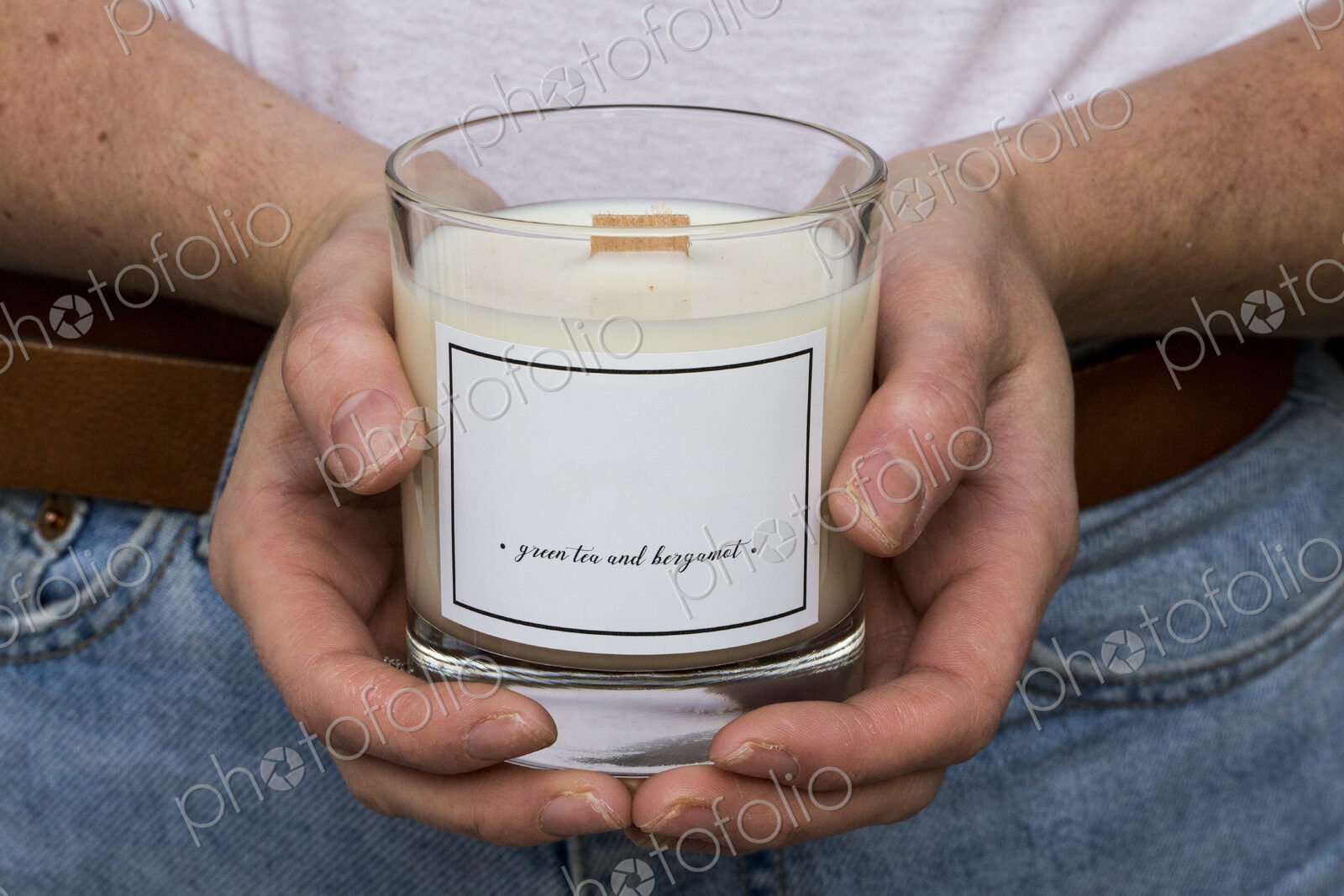 Close up of person holding handmade white and yellow jar candle with wooden wick.