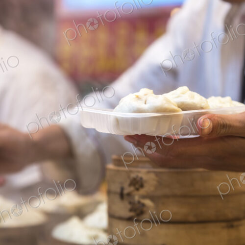 Close up of person holding plate with dumplings and chopsticks.