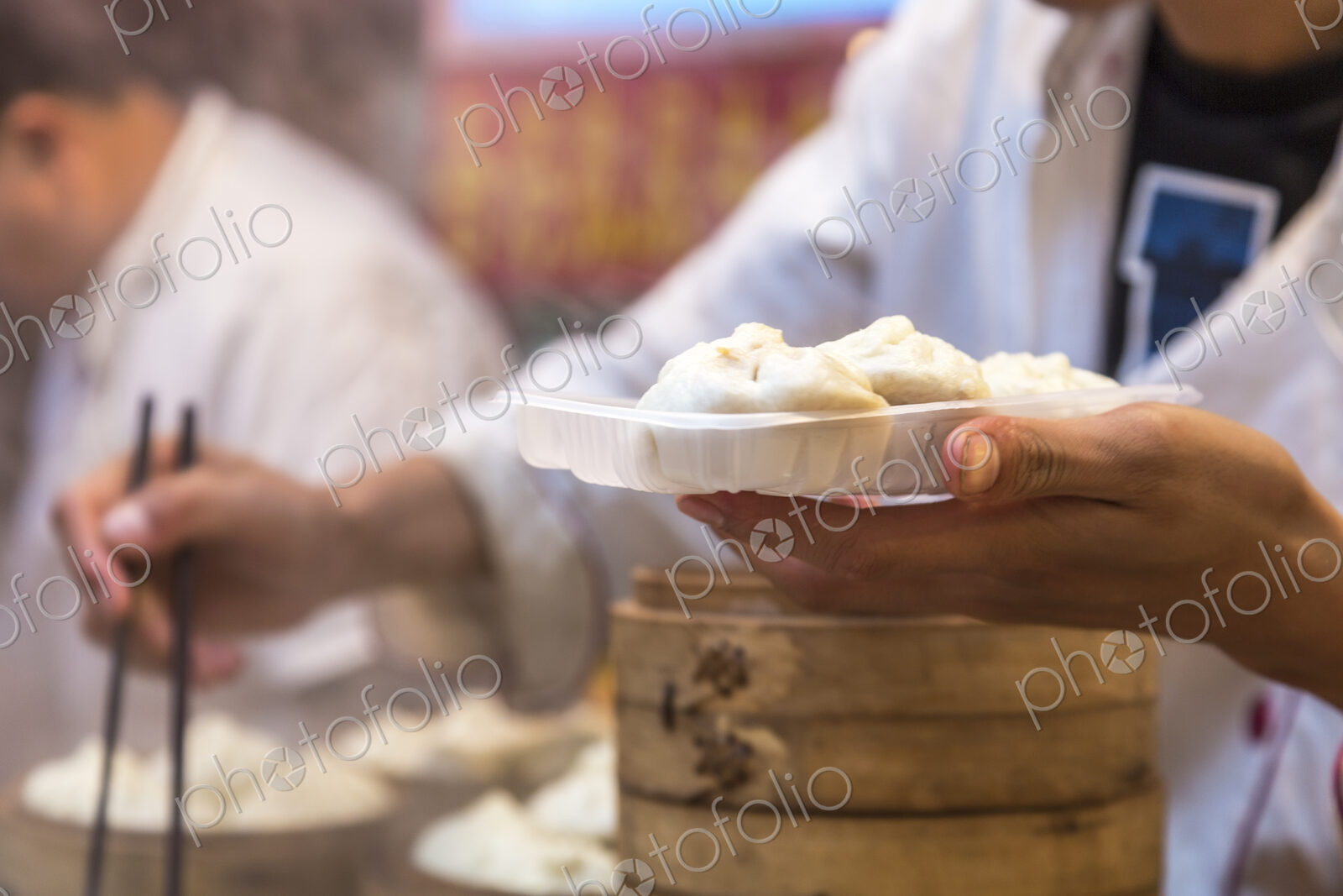 Close up of person holding plate with dumplings and chopsticks.