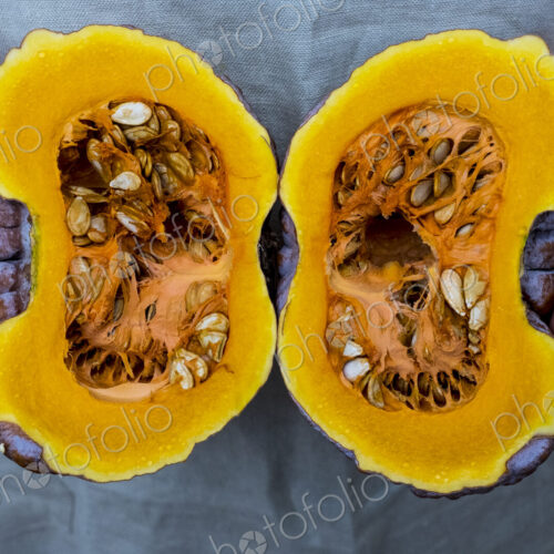 Close up of person holding pumpkin with orange flesh cut in half.