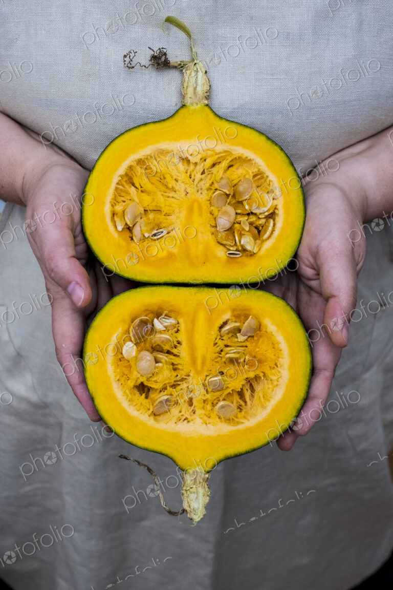 Close up of person holding pumpkin with orange flesh cut in half.