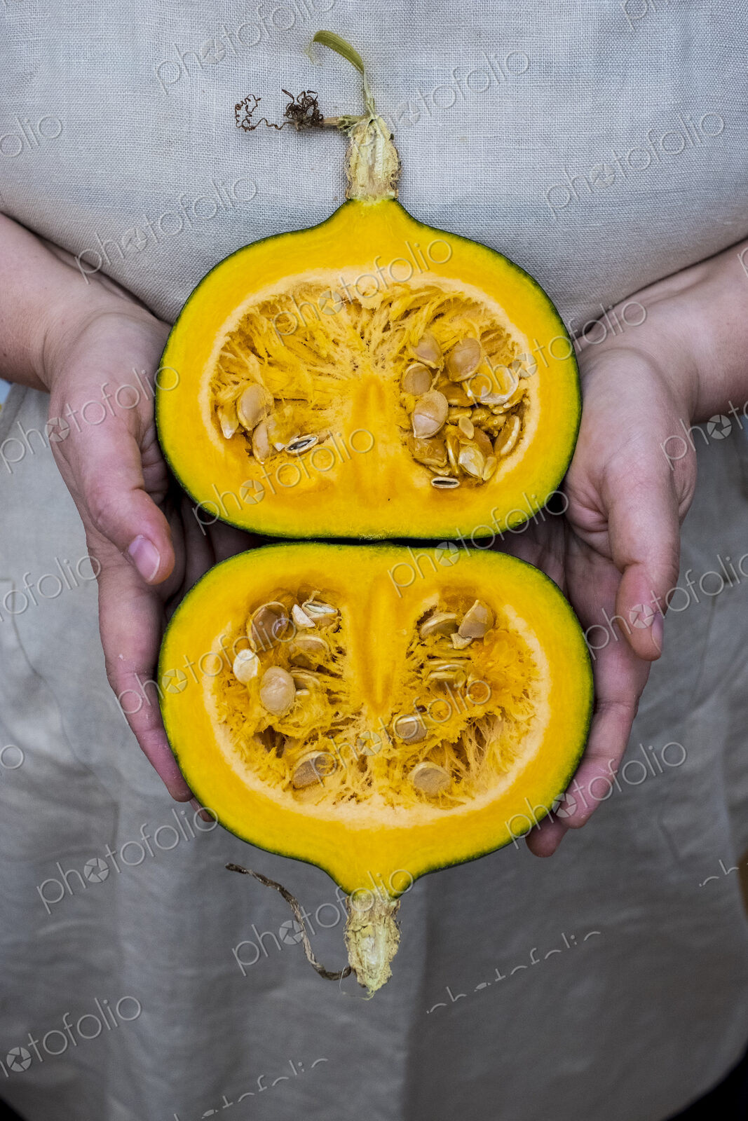 Close up of person holding pumpkin with orange flesh cut in half.