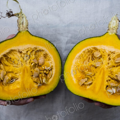 Close up of person holding pumpkin with orange flesh cut in half.