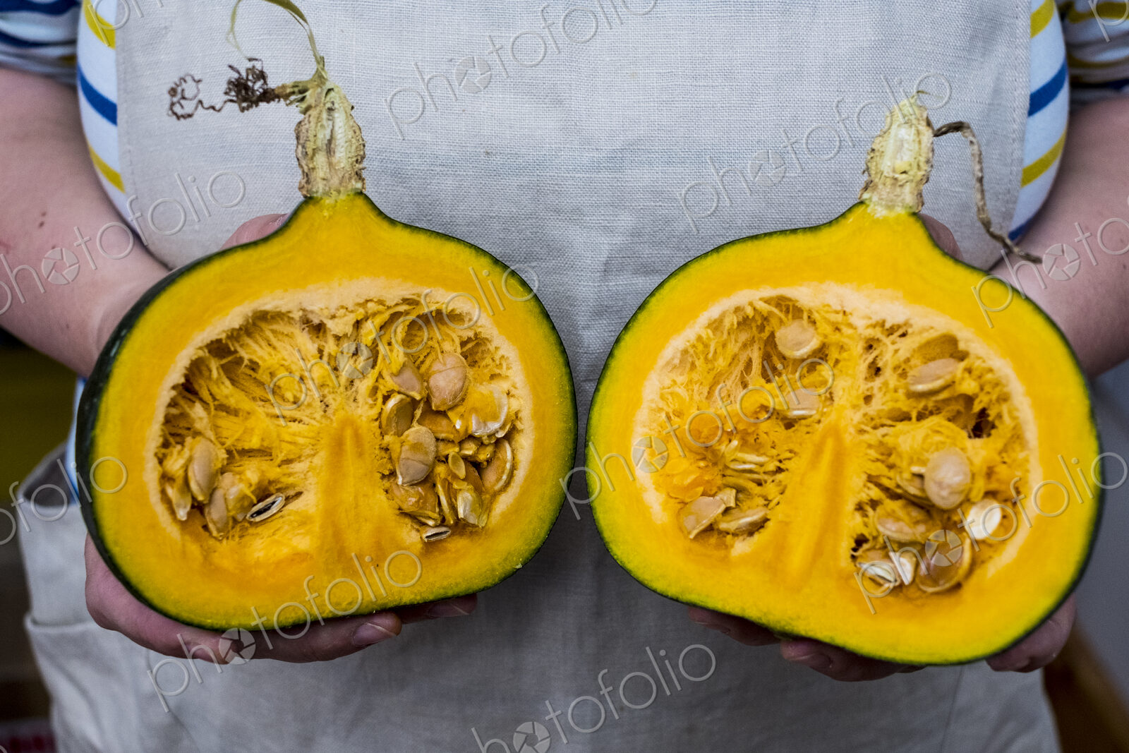 Close up of person holding pumpkin with orange flesh cut in half.