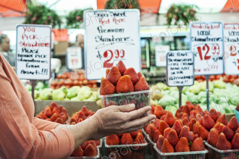 Close up of person holding punnet of fresh strawberries at a fruit and vegetable market.
