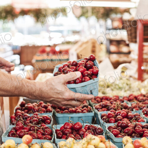 Close up of person holding punnet with fresh red cherries at a fruit and vegetable market.