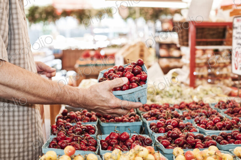 Close up of person holding punnet with fresh red cherries at a fruit and vegetable market.