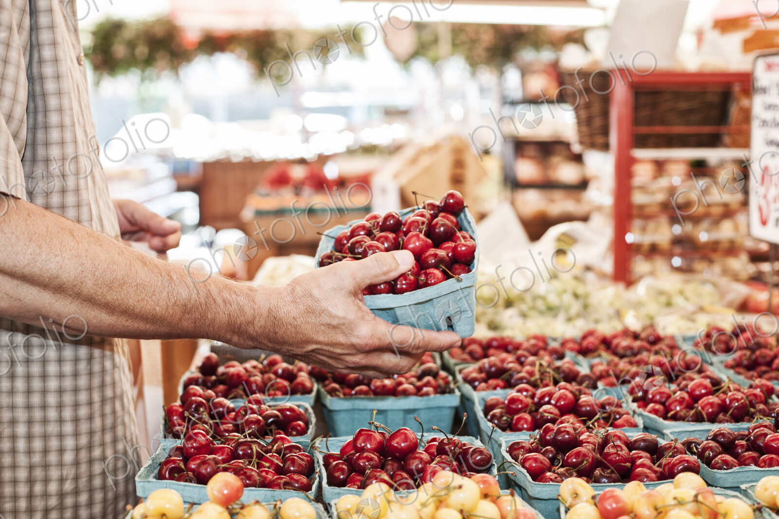Close up of person holding punnet with fresh red cherries at a fruit and vegetable market.