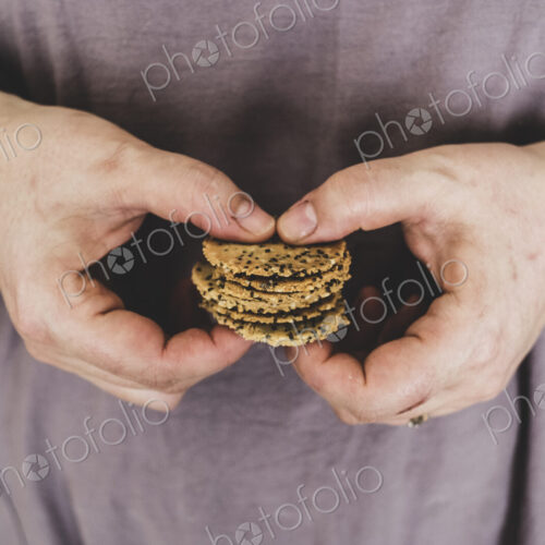 Close up of person holding small stack of freshly baked seeded crackers.
