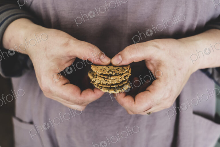 Close up of person holding small stack of freshly baked seeded crackers.