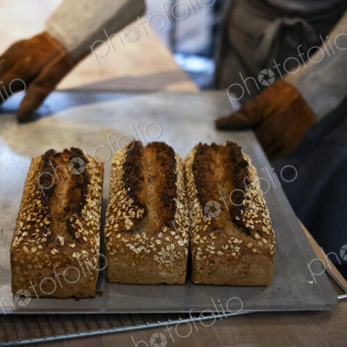 Close up of person holding tray with freshly baked seeded loaves of bread in an…