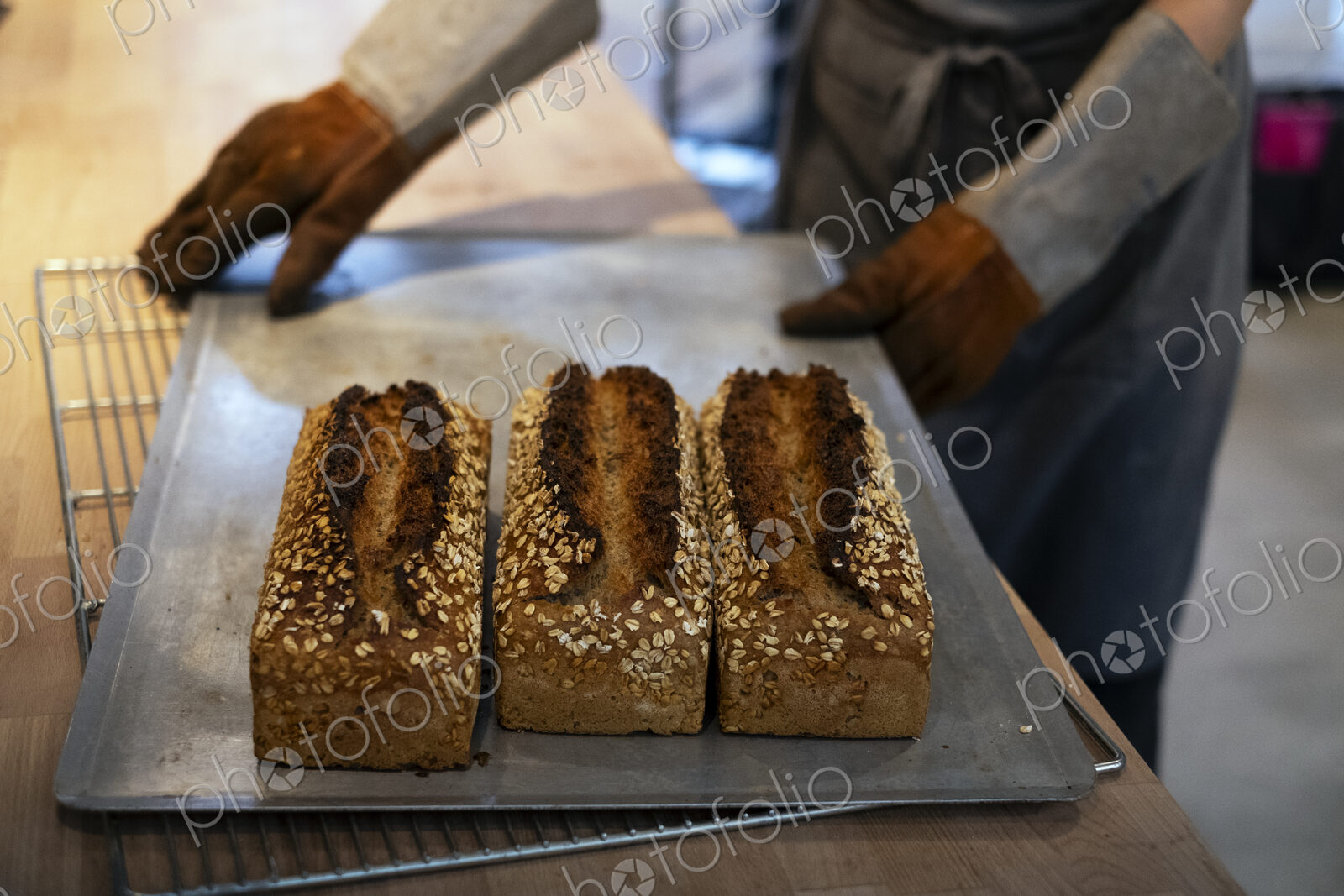 Close up of person holding tray with freshly baked seeded loaves of bread in an…