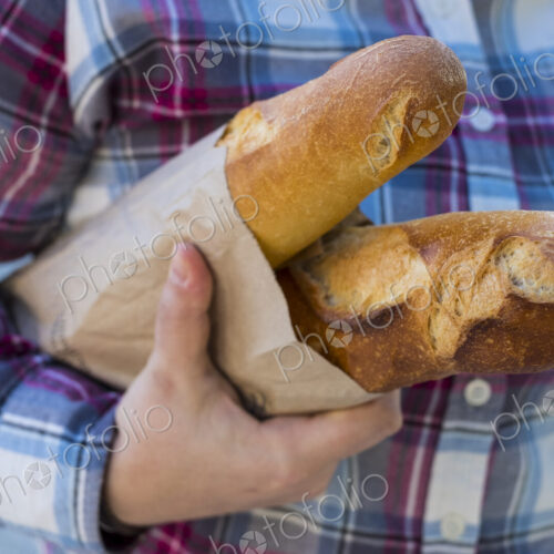 Close up of person holding two freshly baked French baguettes in brown paper bag. Close up of person holding two freshly baked French baguettes in brown paper bag.