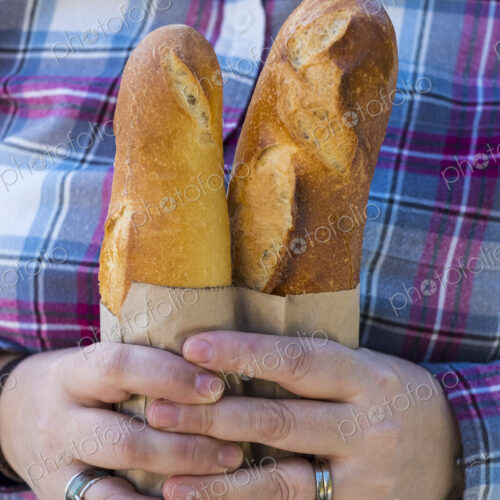 Close up of person holding two freshly baked French baguettes in brown paper bag. Close up of person holding two freshly baked French baguettes in brown paper bag.