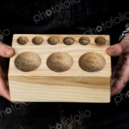 Close up of person holding wooden block with circular holes in different sizes. Close up of person holding wooden block with circular holes in different sizes.