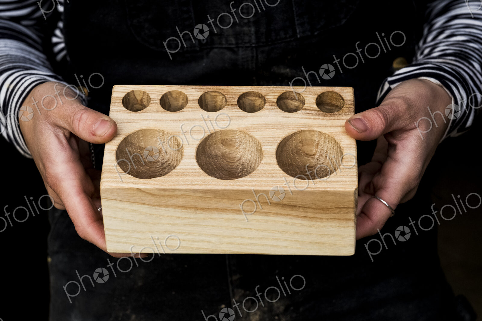 Close up of person holding wooden block with circular holes in different sizes.