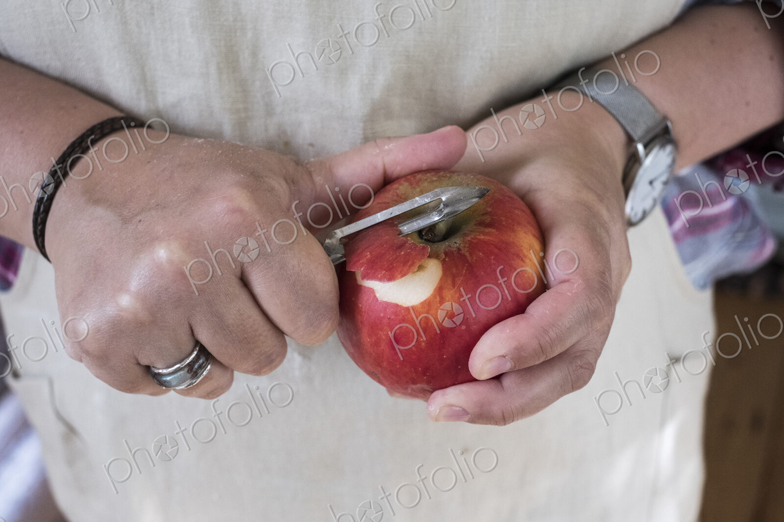Close up of person peeling a red apple with a double bladed peeler.