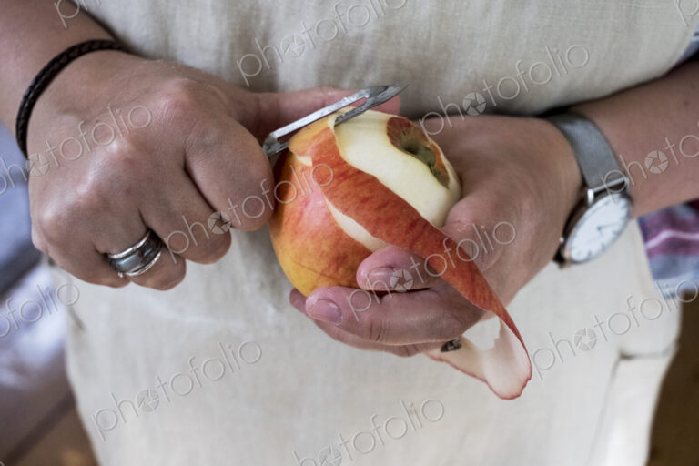 Close up of person peeling a red apple with a double bladed peeler.