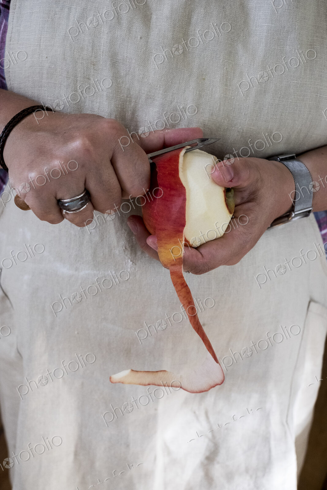Close up of person peeling a red apple with a double bladed peeler.
