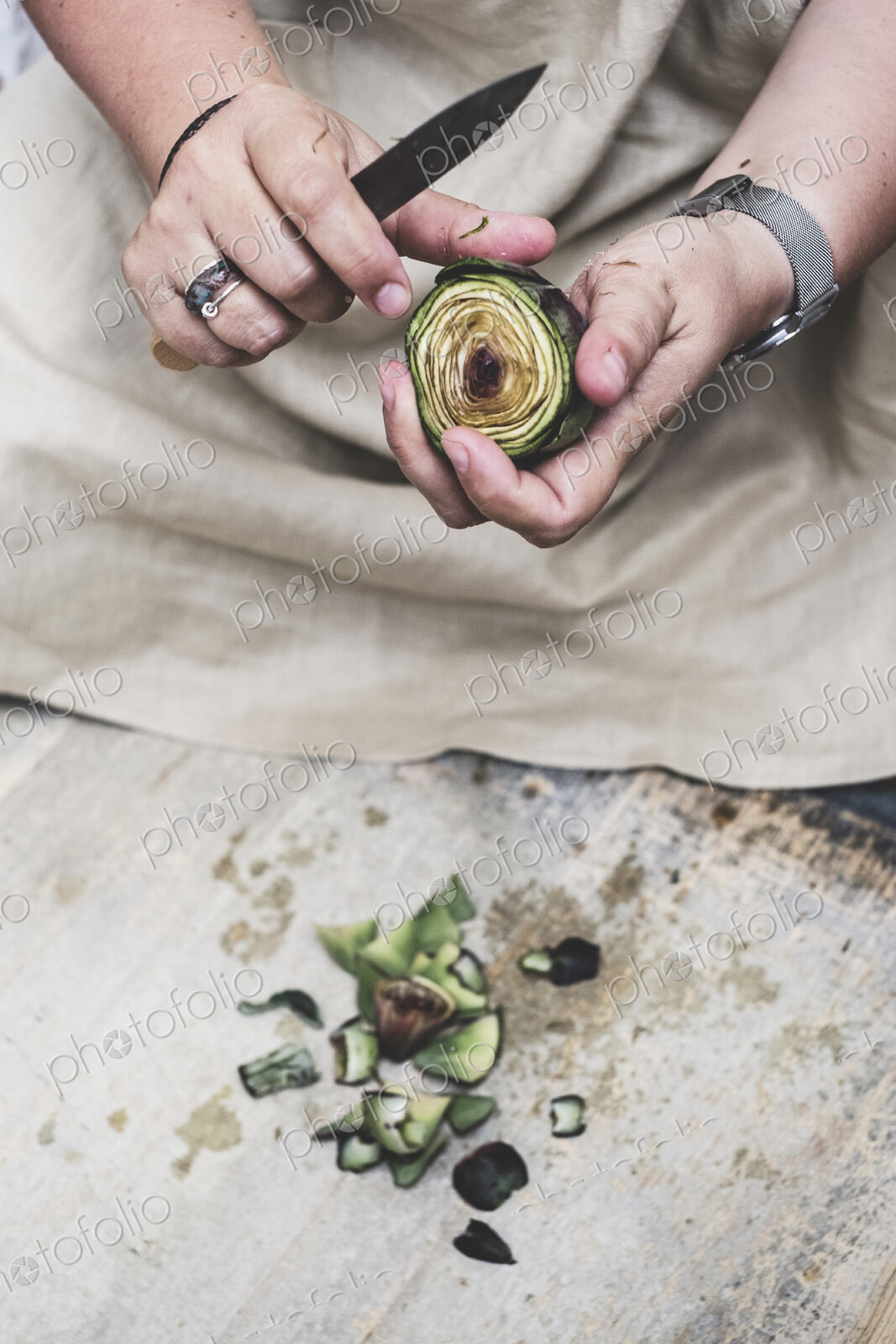 Close up of person peeling fresh artichoke with kitchen knife.