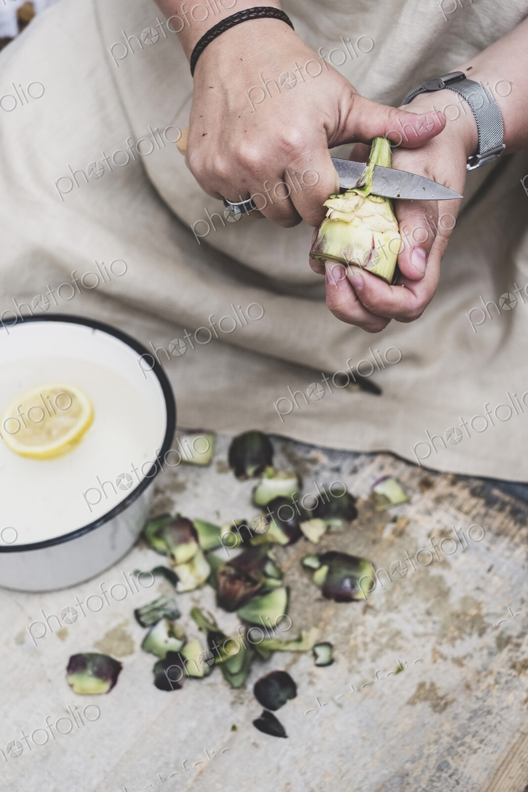 Close up of person peeling fresh artichoke with kitchen knife.