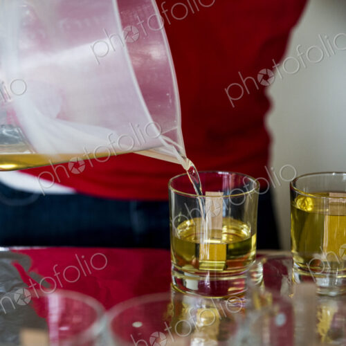 Close up of person pouring liquid wax for handmade candles into glass jars.