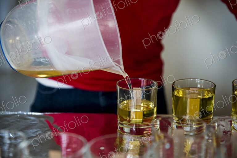 Close up of person pouring liquid wax for handmade candles into glass jars.