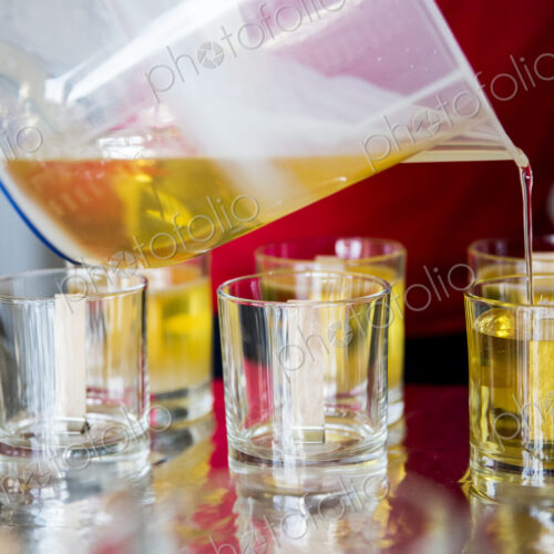 Close up of person pouring liquid wax for handmade candles into glass jars.