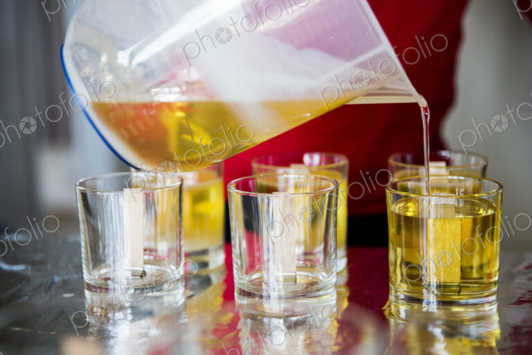 Close up of person pouring liquid wax for handmade candles into glass jars.