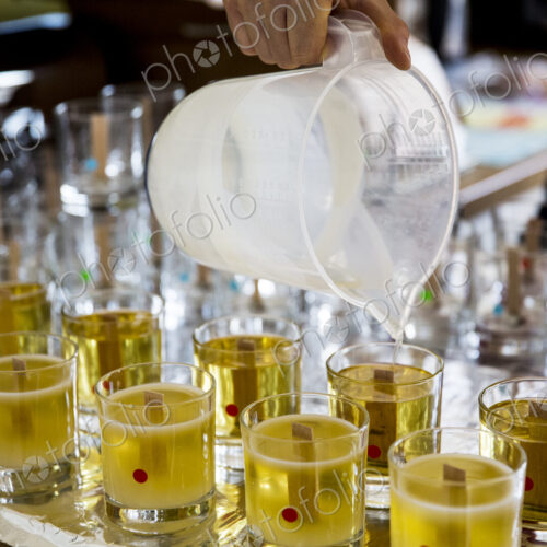 Close up of person pouring liquid wax for handmade candles into glass jars.