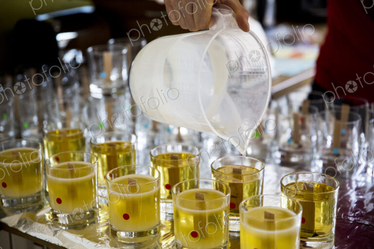 Close up of person pouring liquid wax for handmade candles into glass jars.